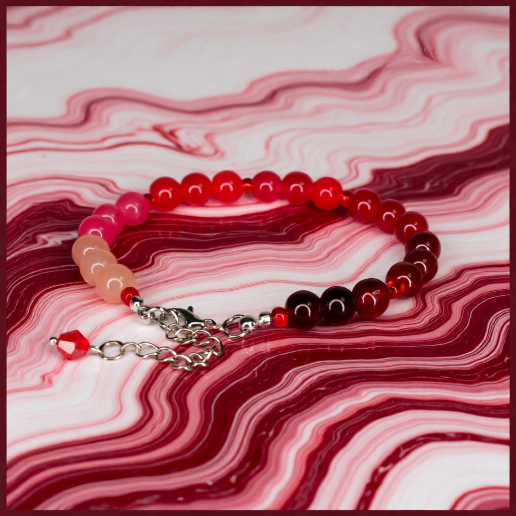Beaded bracelet with red, pink, and silver elements on a marbled pink and red background