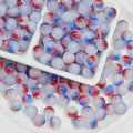 Round glass beads with a swirled red, white, and blue design, displayed in a white divided tray and scattered around it.
