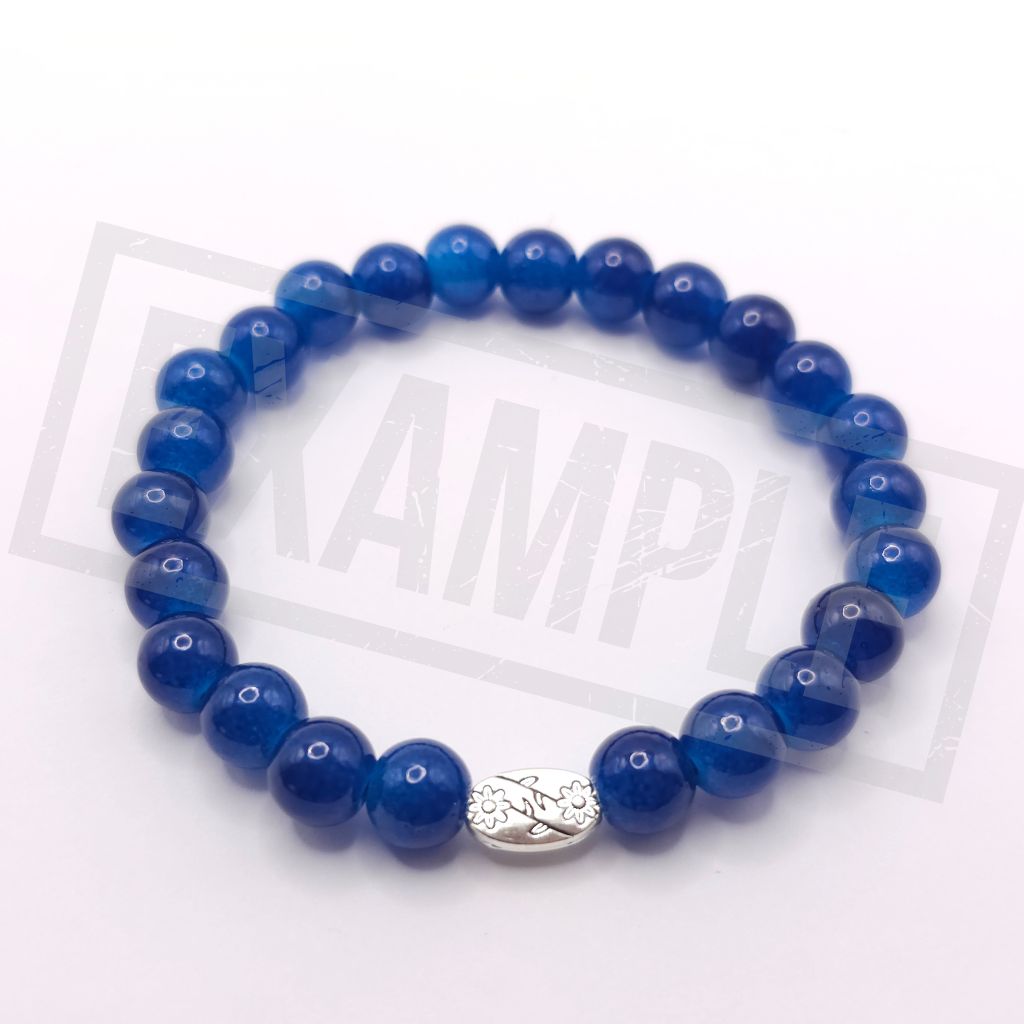 A beaded stretch bracelet made of glossy sapphire blue beads with a small silver-toned decorative charm, shown on a white background.