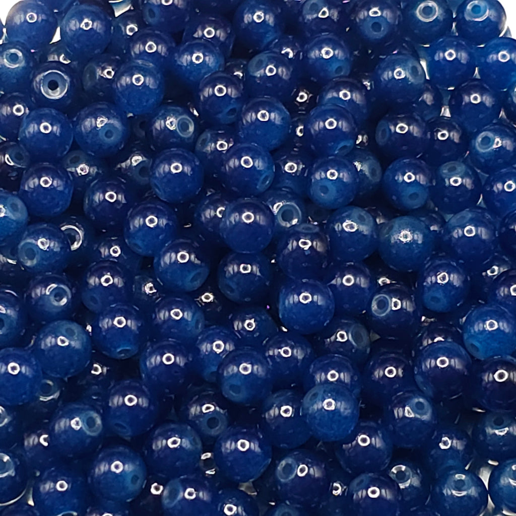 A close-up pile of glossy, deep blue round beads with visible center holes, filling the entire frame.