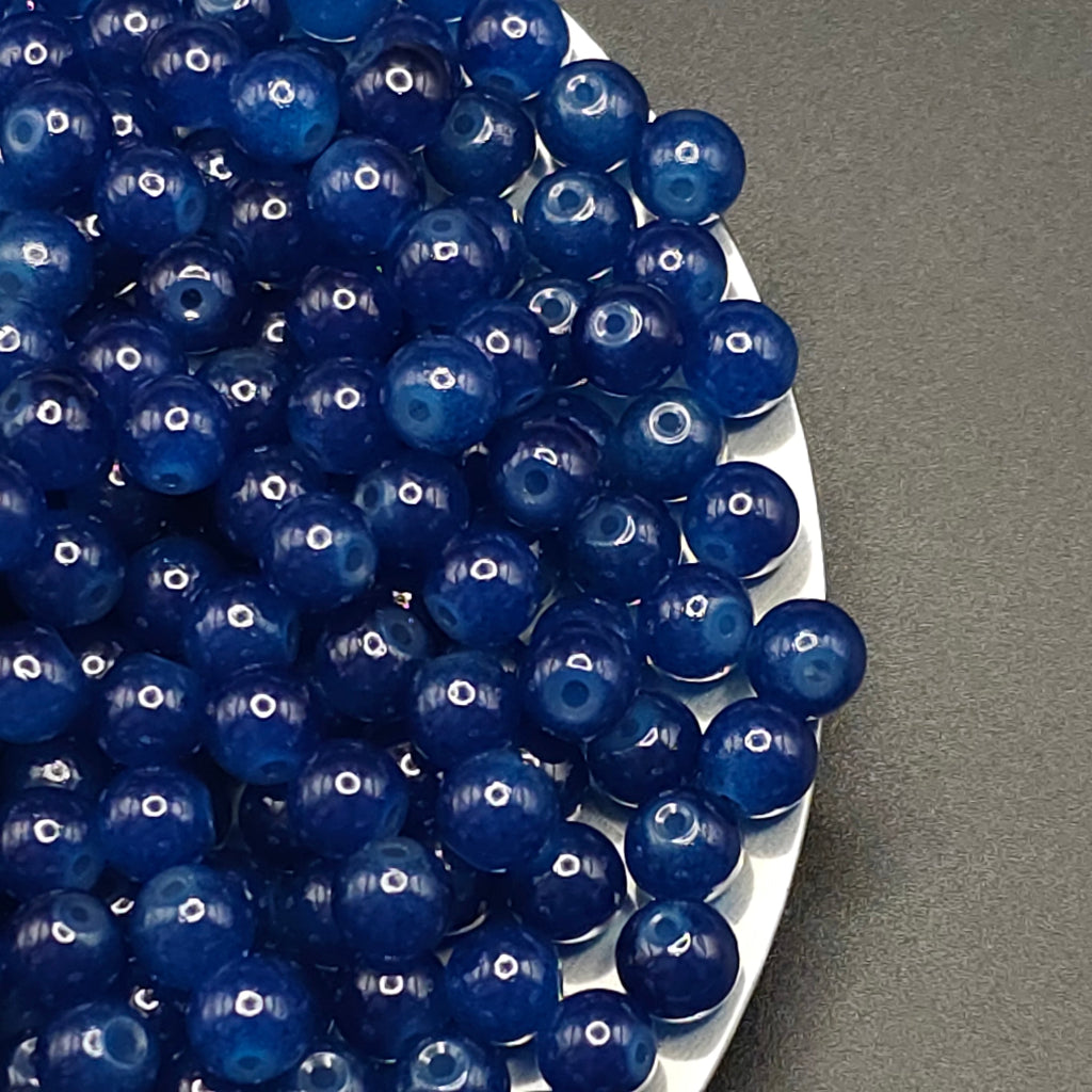 A pile of glossy, deep blue glass marbled beads with a central hole, resting on a white plate against a dark gray background.