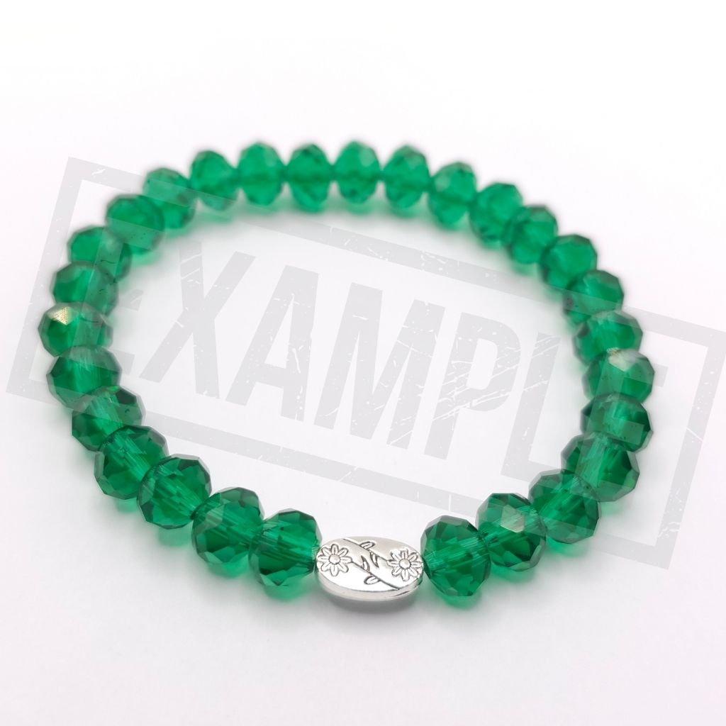 A beaded stretch bracelet made of faceted green beads with a small silver oval charm engraved with flowers, shown on a white background.