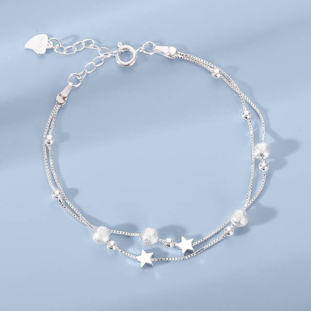 Silver bracelet with star and heart charms on a light blue background