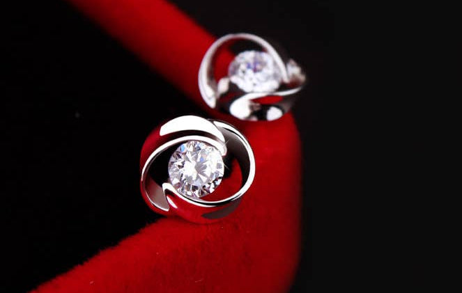 Silver earrings with clear gemstones on a red surface