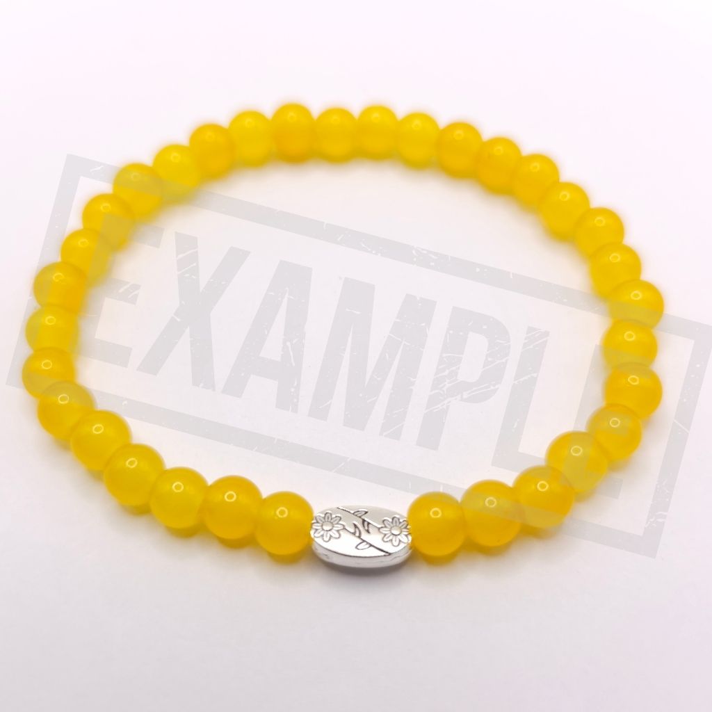 A yellow beaded bracelet with a silver oval charm featuring a floral design, displayed on a white background.