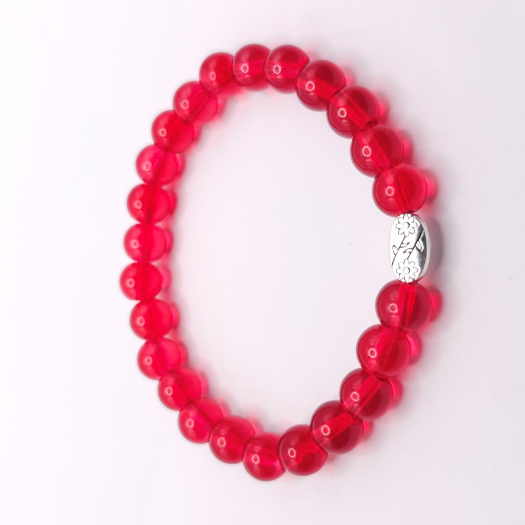 A beaded stretch bracelet made of translucent red glass beads with a small silver-toned metal charm in the center, shown on a plain white background.