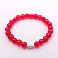 A beaded stretch bracelet made of translucent red glass beads with a small silver-toned metal charm in the center, shown on a plain white background.