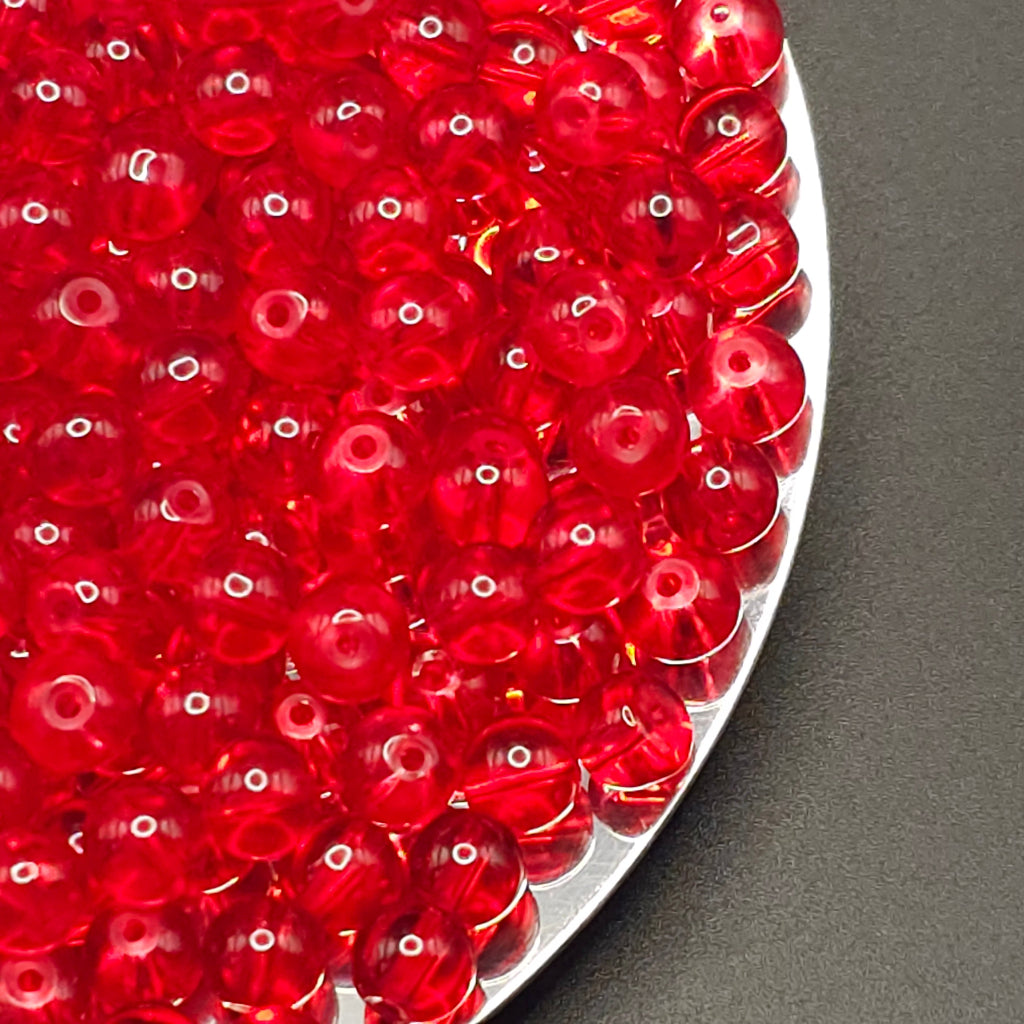 Red translucent round craft beads piled on a silver plate against a dark gray background.