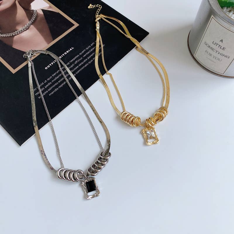 Two necklaces, one silver and one gold, on a white surface with a black box in the background.