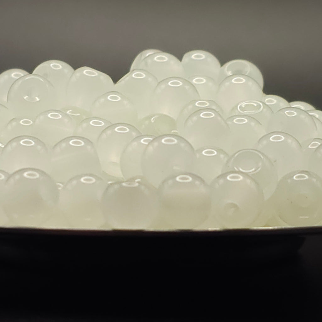 A close-up of many small translucent white oval beads or pearls piled in a dark dish against a dark gray background.