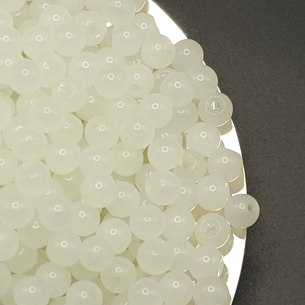 A pile of small translucent white round beads with a single hole, shown close up on a dark gray surface.