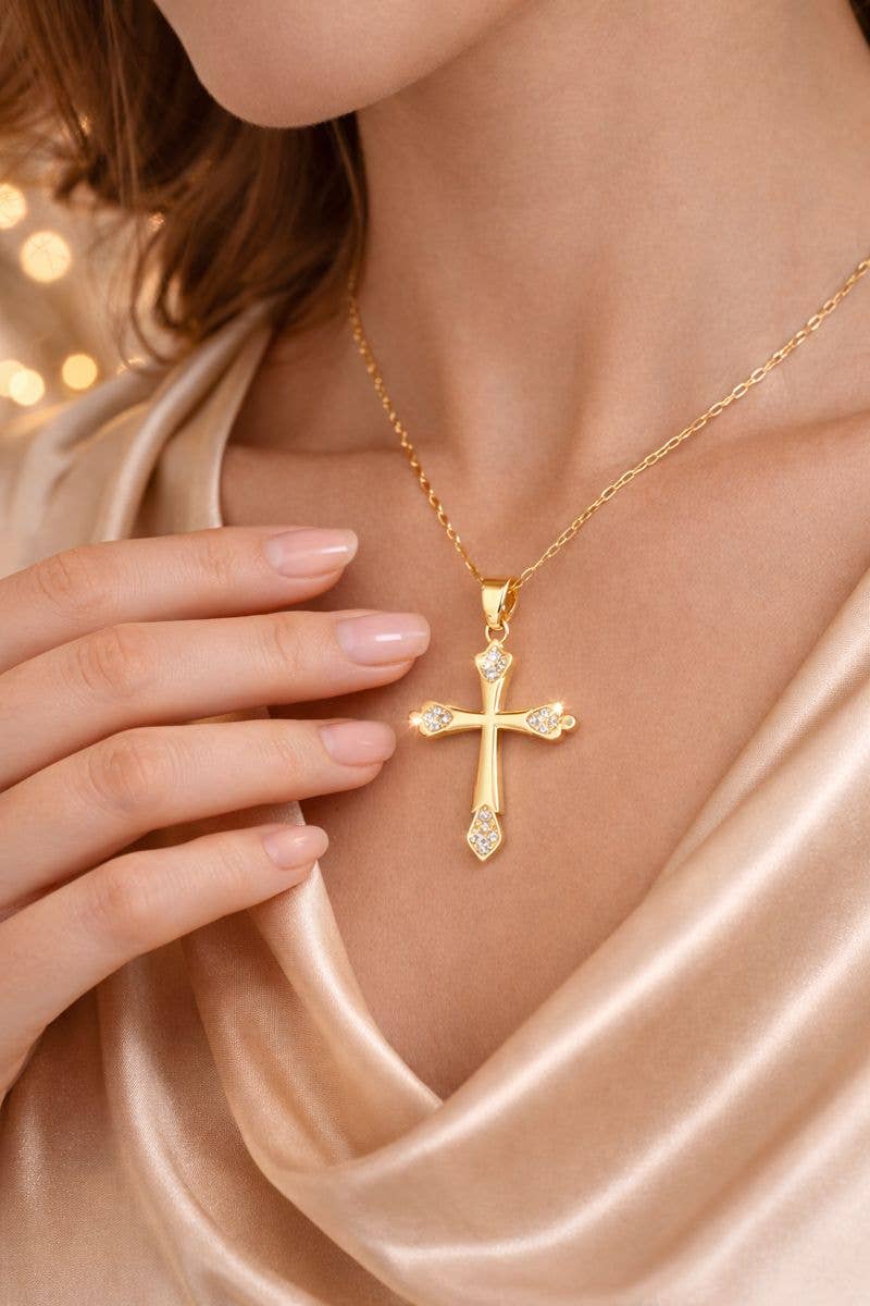 Gold cross necklace with diamonds on a person wearing a beige garment.