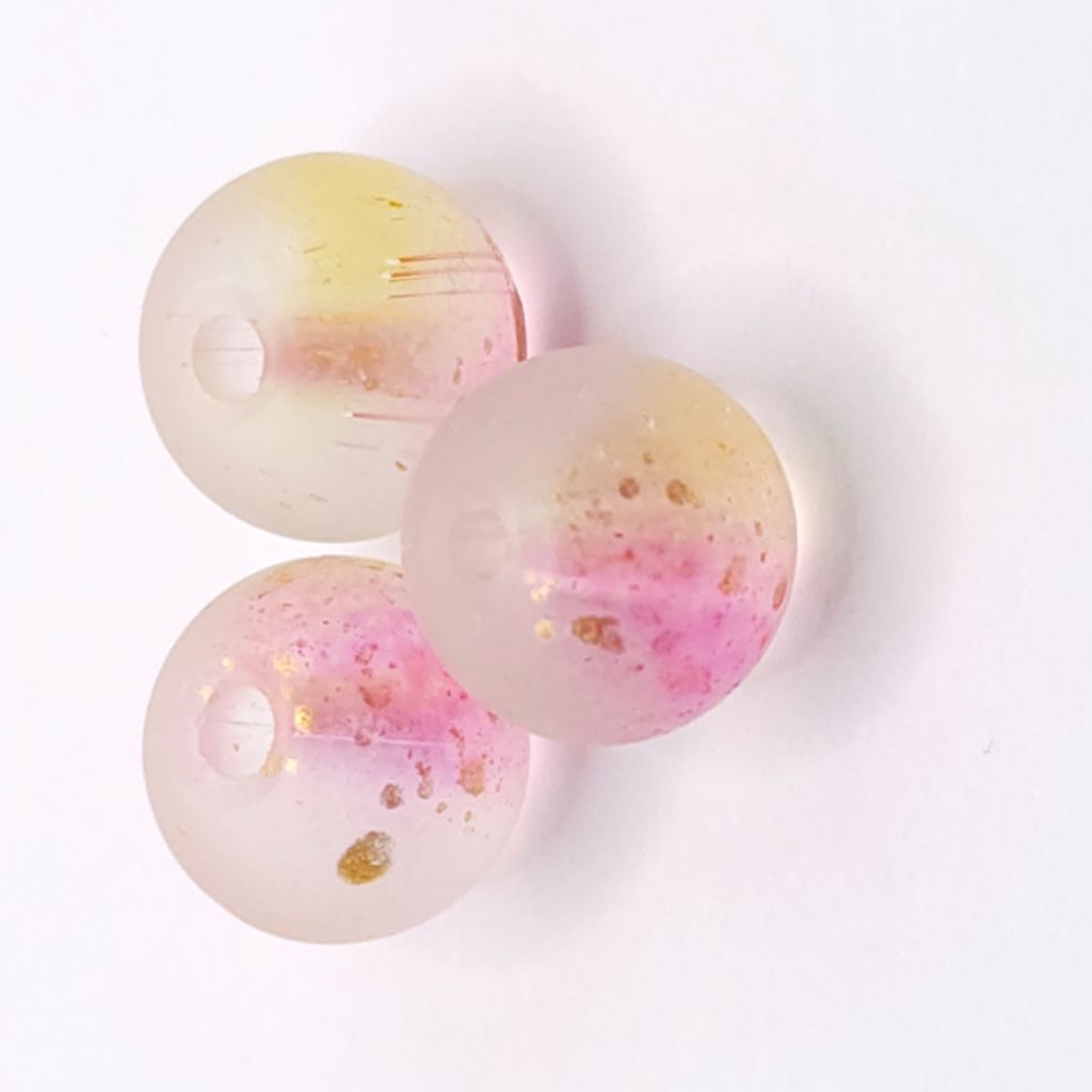 Three round translucent glass beads with pink and pale yellow color gradients, containing small gold foil flakes, arranged on a white background.