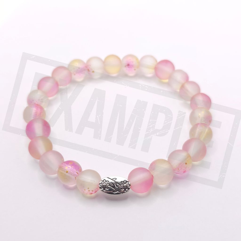 A beaded stretch bracelet made of translucent pink and pale yellow glass beads with small floral details, featuring a silver-toned decorative accent bead in the center, shown on a white background .