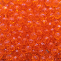 A pile of small, faceted orange glass beads arranged in a mound on a dark round surface against a white background.